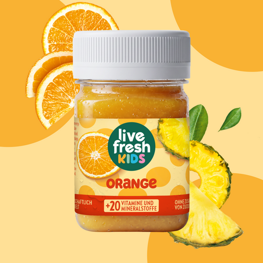 LiveFresh Kids Orange im Glas vor orangefarbenem Hintergrund mit frischen Orangenscheiben und Ananasstücken. Auf dem Etikett steht "live fresh KIDS". "ORANGE" und "+20 VITAMINE UND MINERALSTOFFE".